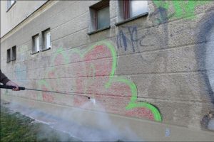 Probíhající odstraňování ošklivého graffiti na fasádě bytového domu.